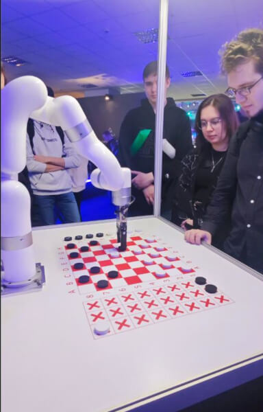 Гости наблюдают за партией в шашки с роботом-манипулятором